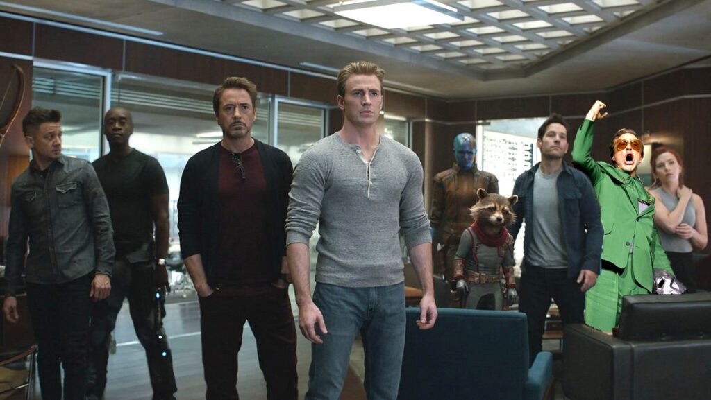 The Avengers standing in a room looking nervous with a yelling Robert Downey Jr. in a green suit photoshopped in