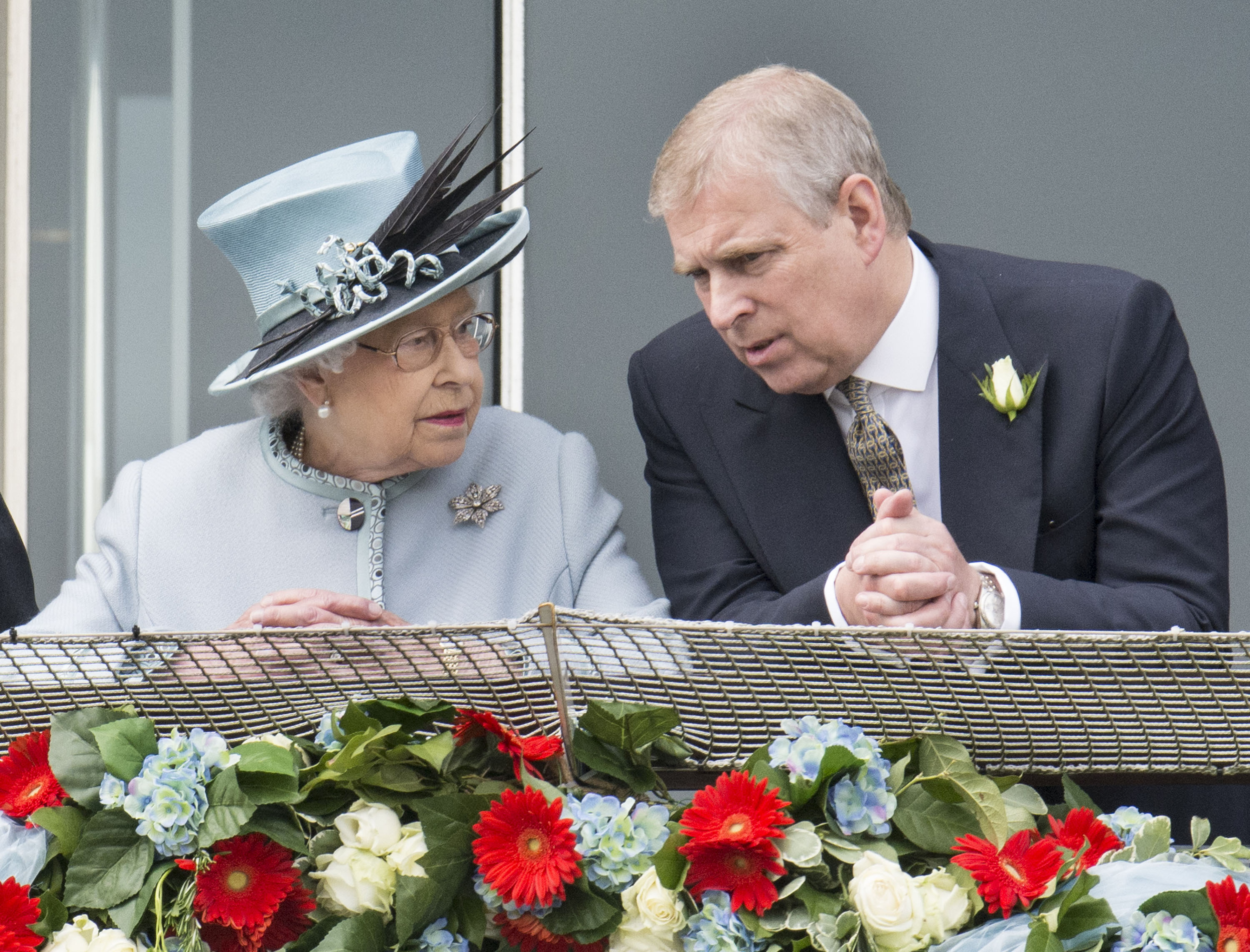 Queen Elizabeth wearing a pale blue coat and hat talking to Prince Andrew on a balcony