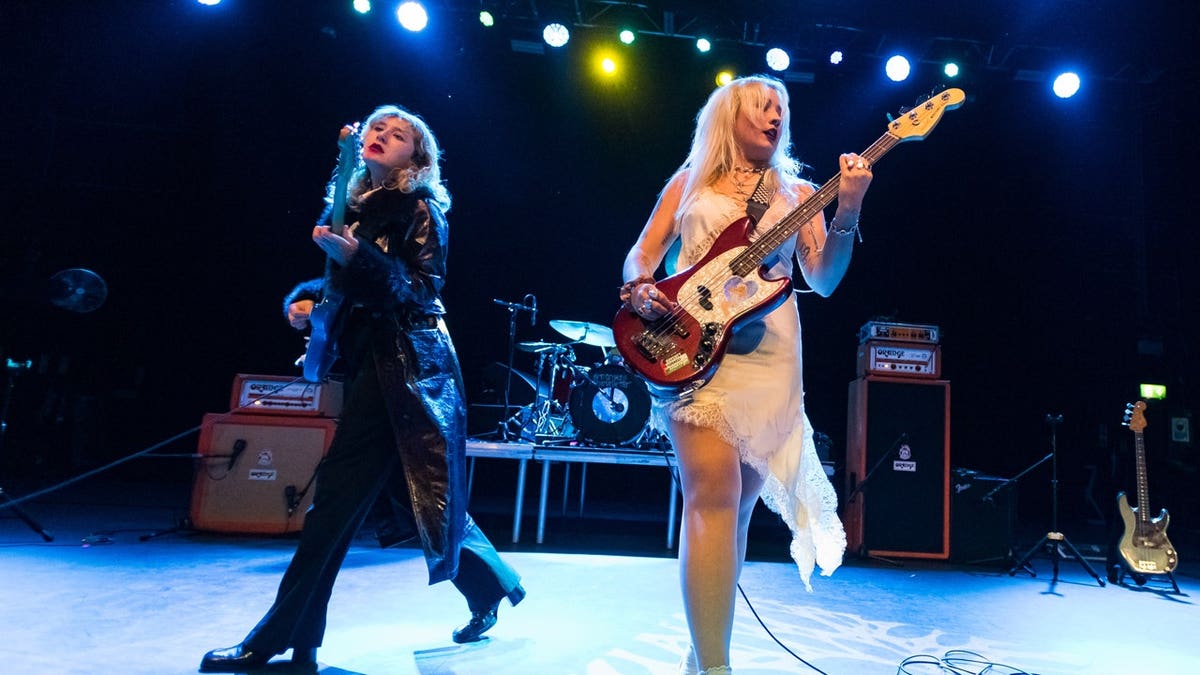 Phoebe Lunny and Selin Macieira-Boşgelmez of Lambrini Girls performing together onstage during a concert.