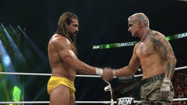Andrade and Darby Allin shake hands in a display of respect after their match at AEW Dynasty. Andrade is wearing yellow trunks, and Darby has an athletic look with multiple tattoos and a mohawk hairstyle.