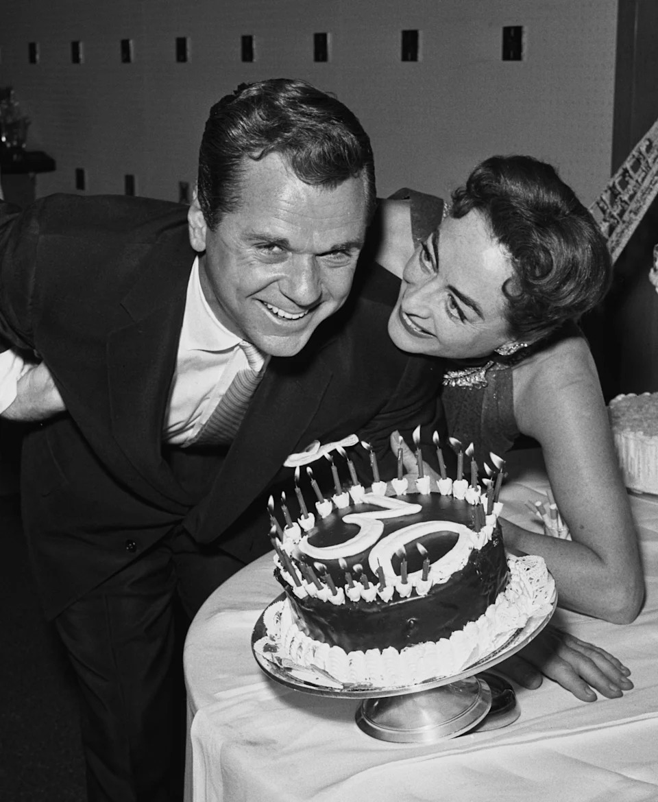 Jackie Cooper and Joan Crawford smile beside a birthday cake at a party