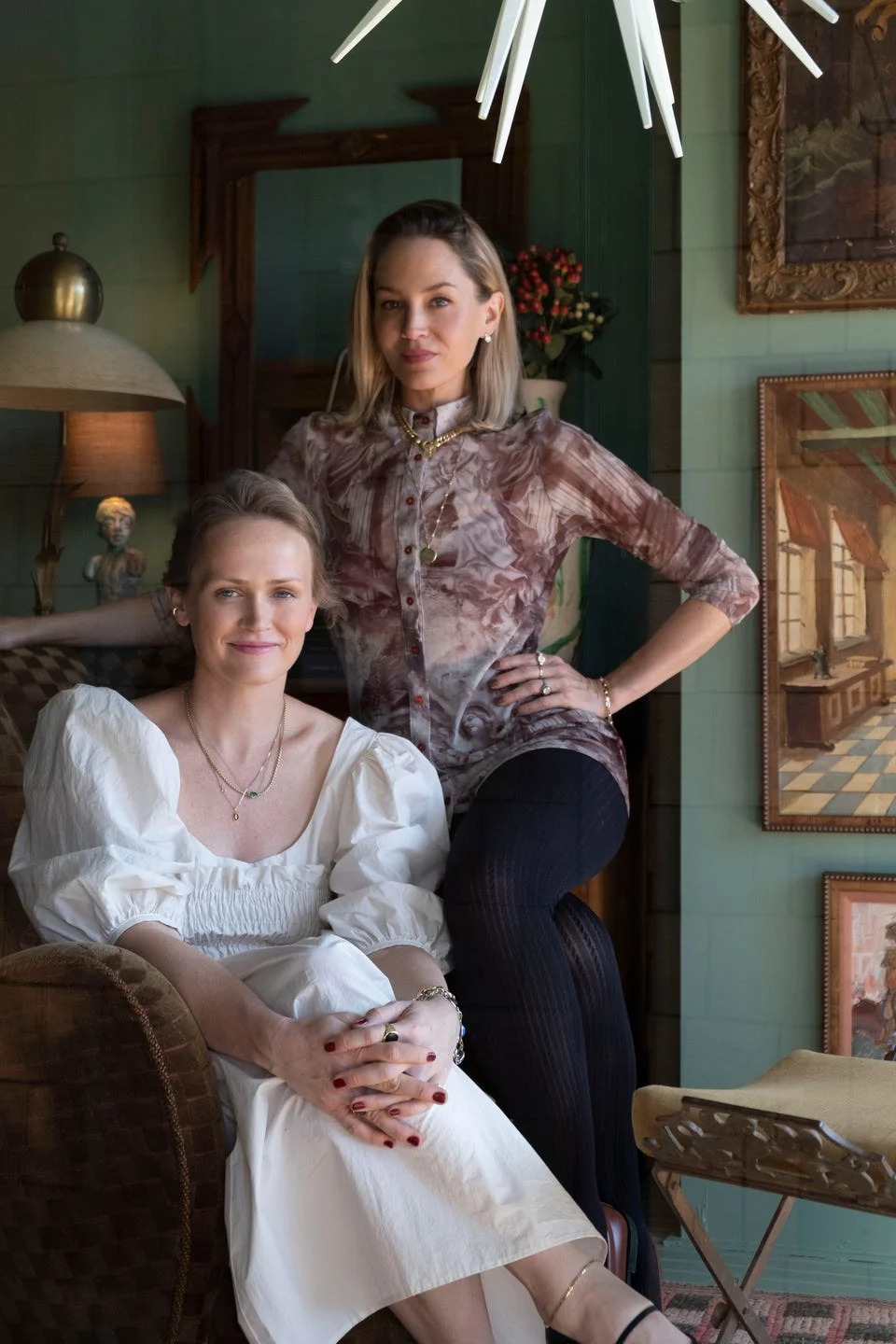 Two women posing in a styled interior space.