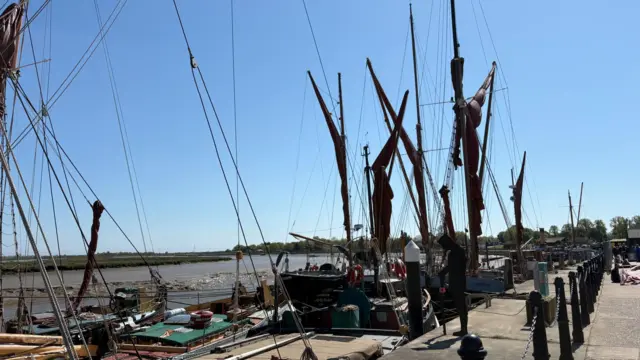 A quayside has several boats lined up against a blue sky