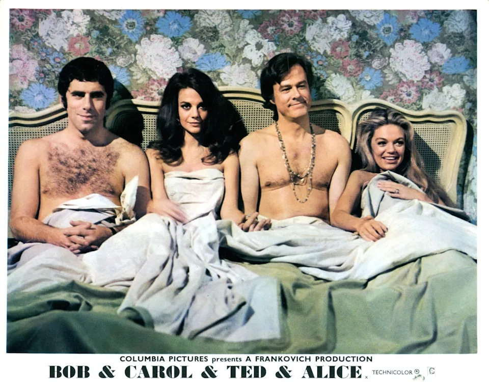 Four people in bed from a scene in the film "Bob & Carol & Ted & Alice," with vintage style hair and sheets up to their chests