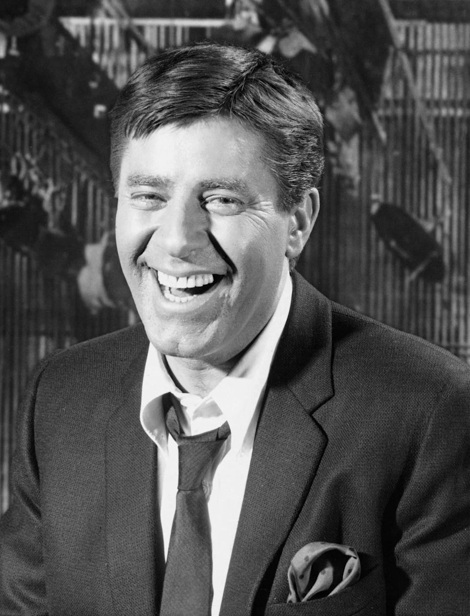 Jerry Lewis in a suit and tie, standing against a blurred background