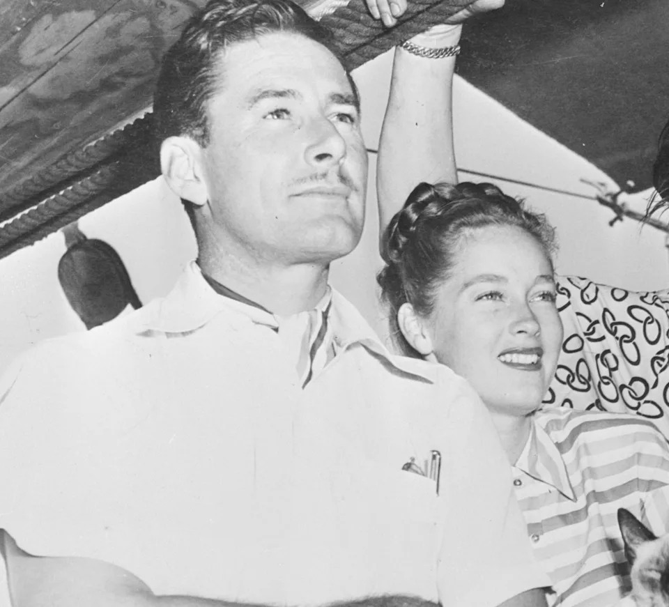 Four people, including one holding a cat, stand on a boat deck under a canopy, looking outward