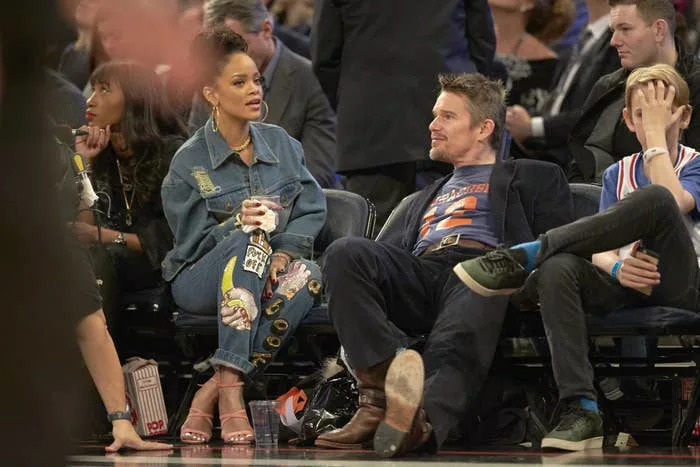 People seated courtside at a basketball game, wearing casual and stylish denim outfits, engaged in conversation and enjoying the event