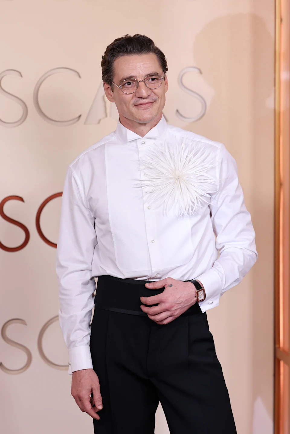 A person on the red carpet wearing a white shirt with a feather detail and dark trousers
