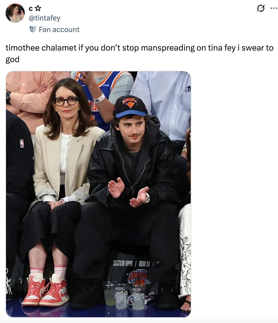 A person sitting courtside at a basketball game, wearing a jacket and beanie, sits next to others, including someone resembling Tina Fey