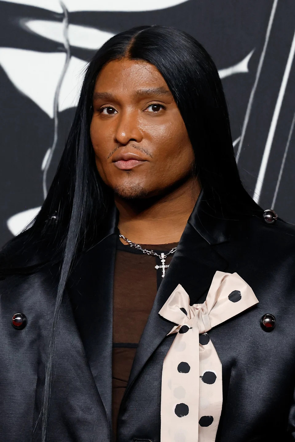 Person on the red carpet wearing a black satin jacket with a polka dot bow detail and long, sleek hair