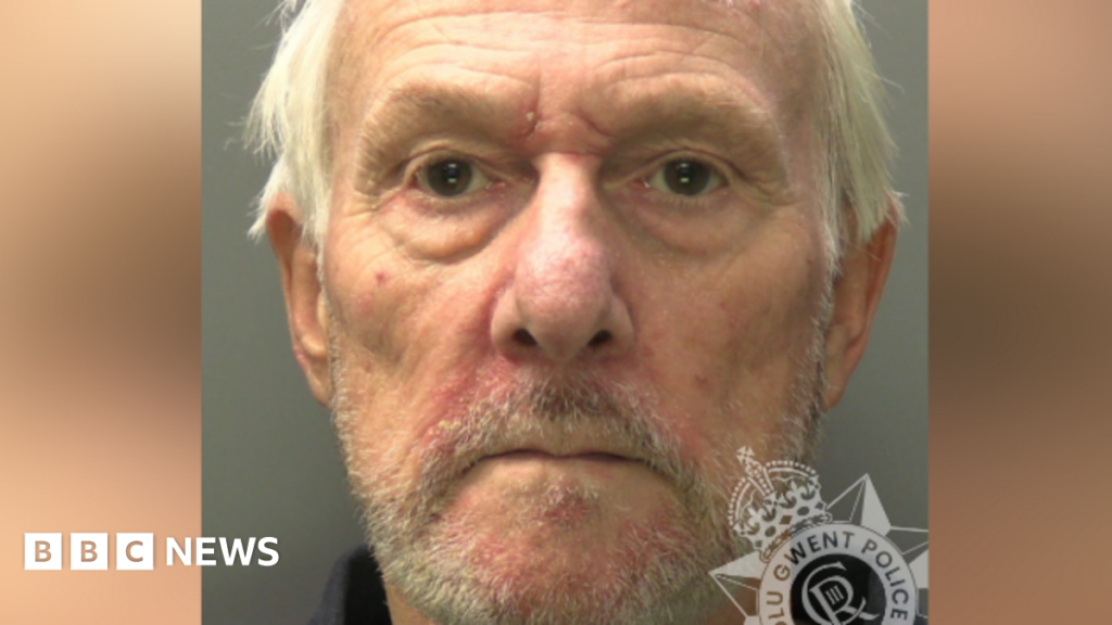 A police custody image of Peter Rowell. He is in his 60s with messy grey hair and short grey stubble. The collar of a dark shirt is visible. Gwent Police's Logo sits in the bottom right-hand corner.