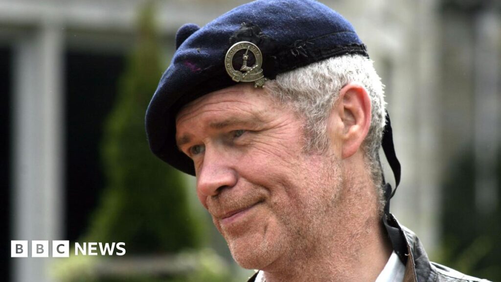 Sandy Morton, smiling in close-up in a tartan hat. He has grey hair.