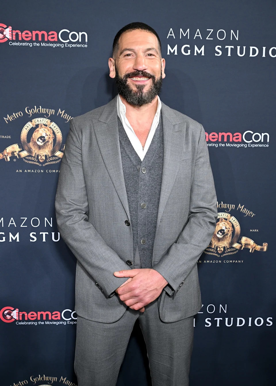 A man on the red carpet in a gray suit with a vest, attending a CinemaCon event