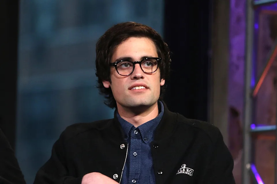 Nick Reiner with glasses and medium-length hair wears a button-up shirt and a casual jacket, looking slightly to the side