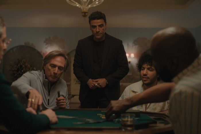 Troy and Benny play poker, while Josh stands between them observing