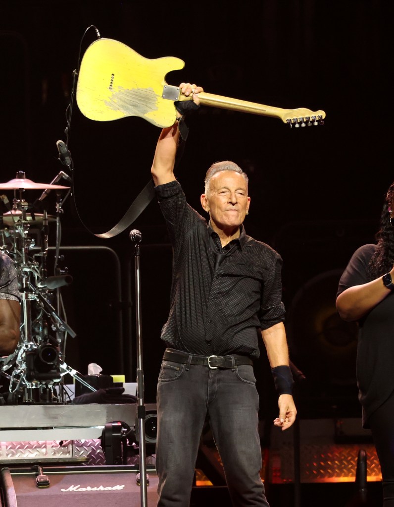 Bruce Springsteen holding up a yellow electric guitar on stage at the Land of Hope & Dreams American Tour in Minneapolis.