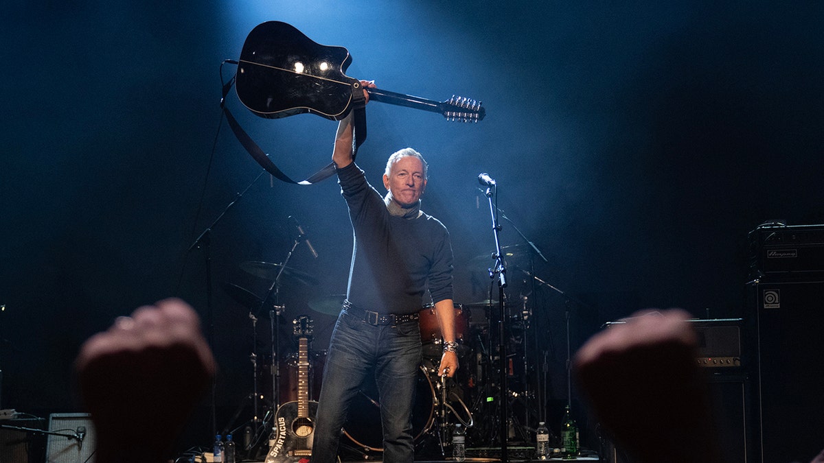 Bruce Springsteen holding guitar above head while performing on stage