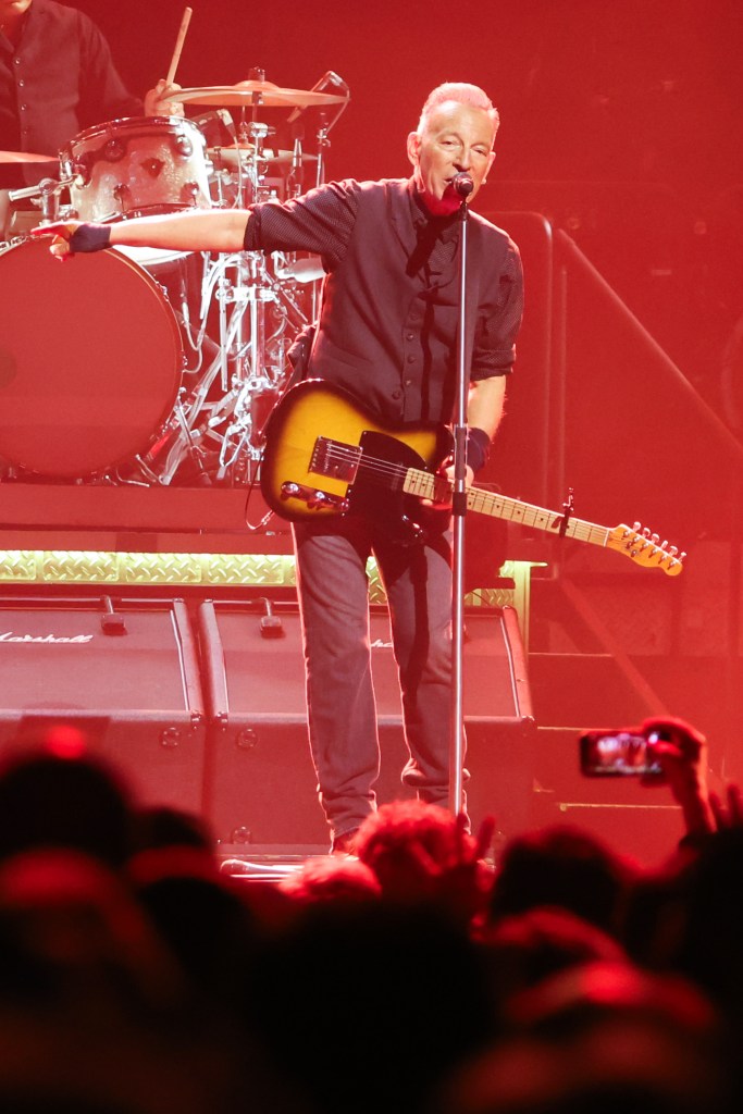 Bruce Springsteen performing live, holding a guitar and singing into a microphone.