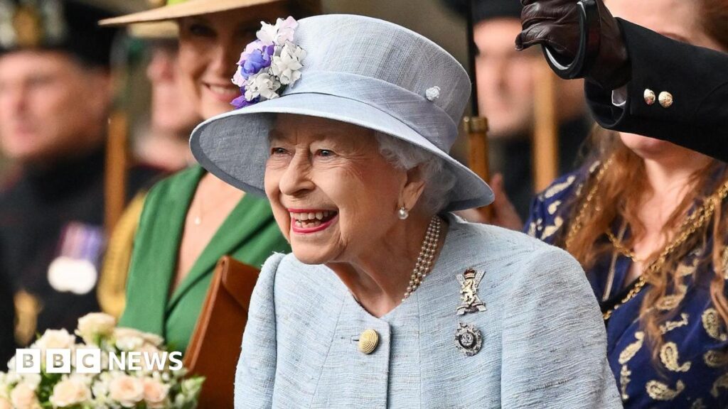 King Charles III with his late mother, Queen Elizabeth II - both are smiling off camera, and standing on the Buckingham Palace balcony which can just be seen. The late Queen wears an emerald green hat and jacket, with pearls and a diamond brooch in the shape of a bow, while the King has a navy pin-striped suit and a pale blue patterned tie