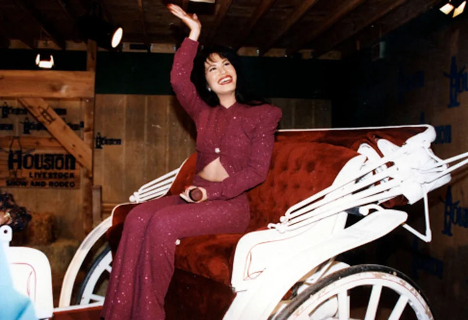 Selena in sequined suit sitting on a carriage, smiling and waving at an event