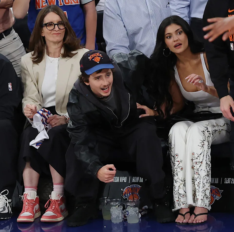 People sitting courtside at a basketball game, reacting to the action. They are casually dressed in jackets and casual attire