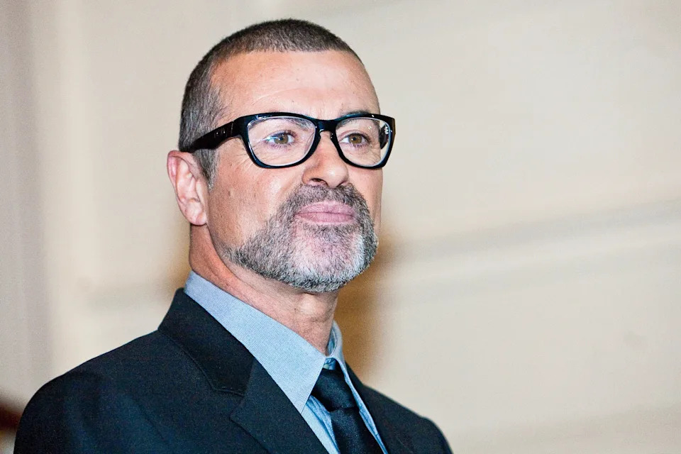 Georgie Michael in formal attire and glasses poses for a photo