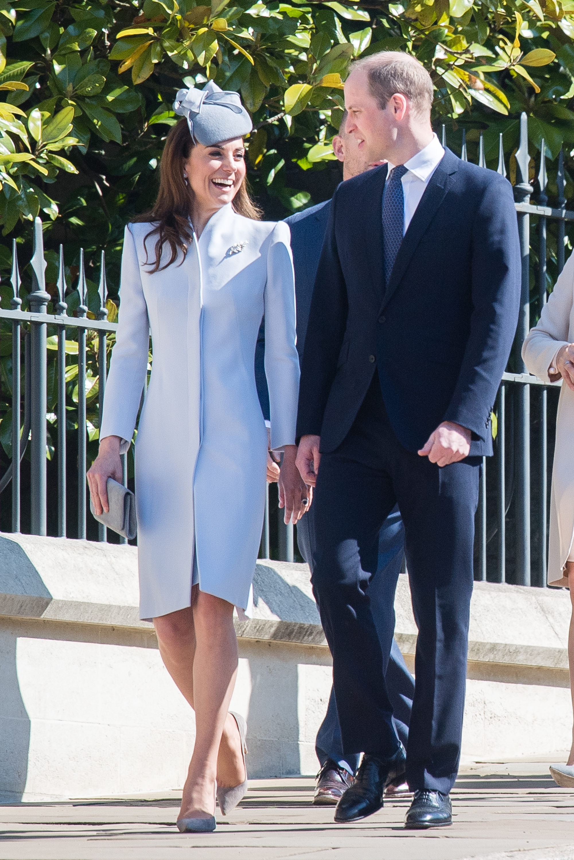 Princess Kate smiling in a gray coat walking next to Prince William