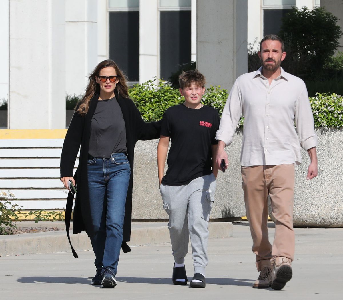 Samuel, dressed casually, walked between his parents, appearing comfortable and engaged.