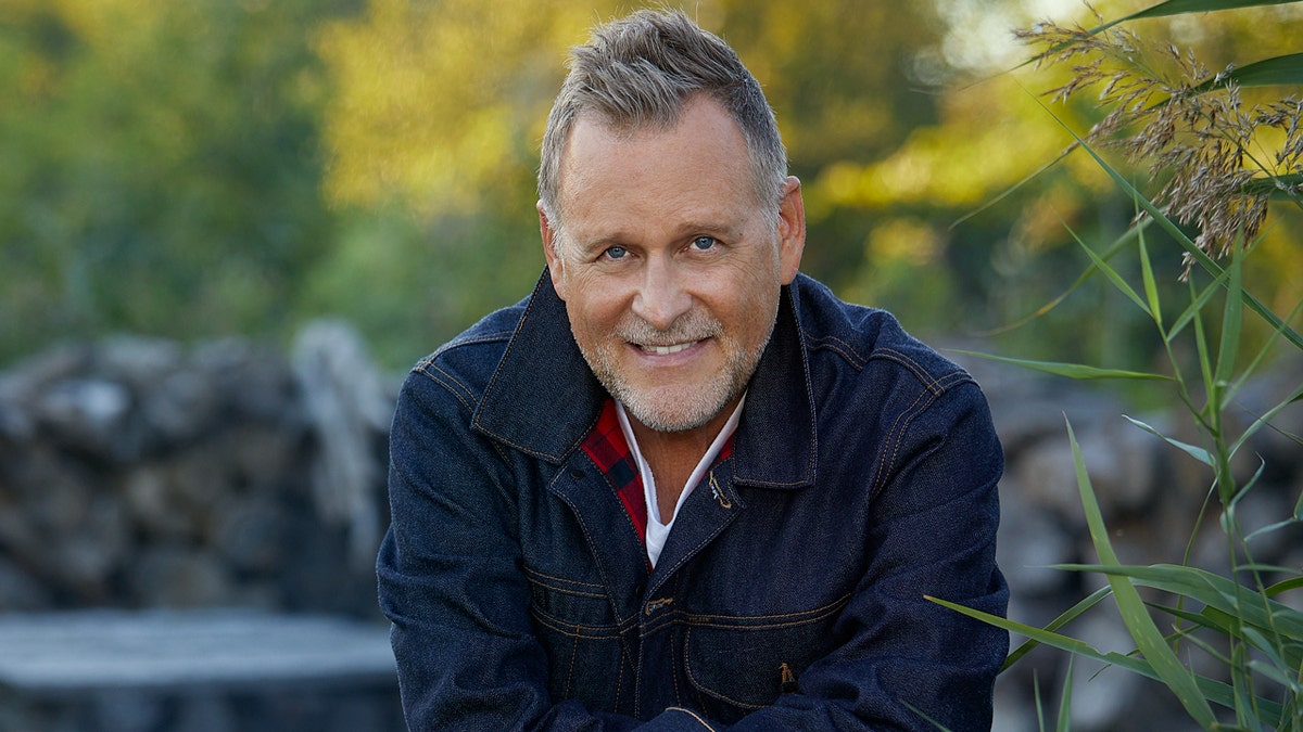 Dave Coulier sitting by a fire outdoors