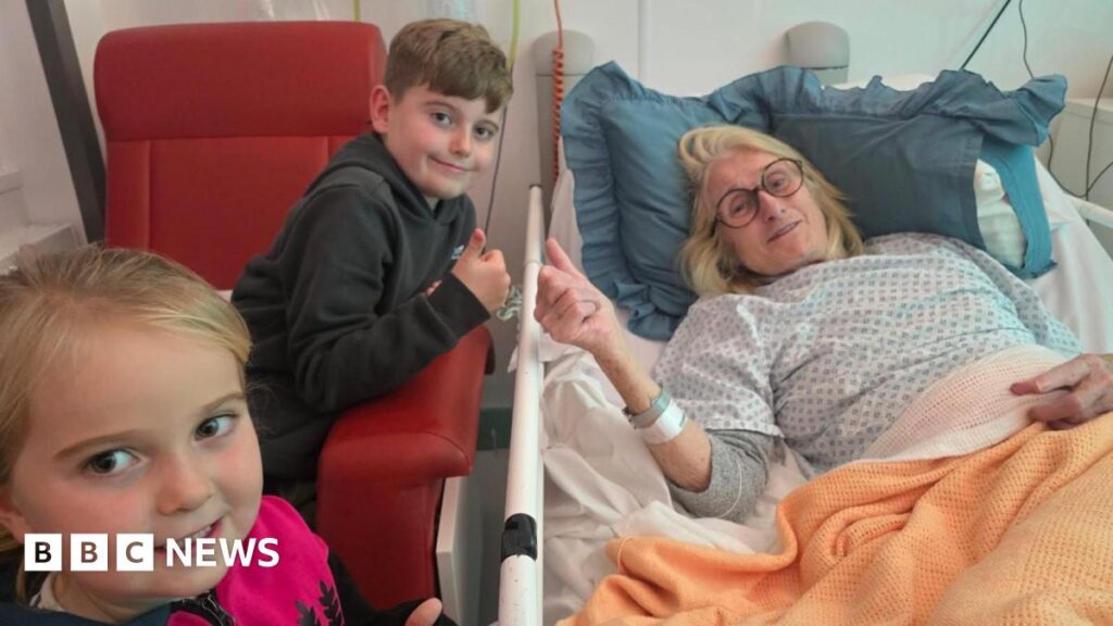 Cold sore virus leaves Penrhyn-coch woman with encephalitis brain damage Helen in a hospital bed with her two grandchildren standing next to her. She wears a hospital gown and has a orange blanket over her. A young boy sits on a red chair next to her with his thumb up, and a young girl with blonde hair smiles at the camera.