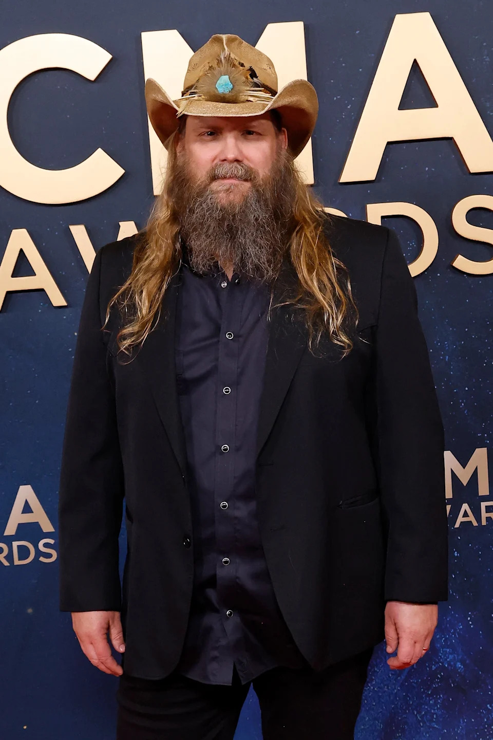 Man in cowboy hat and suit at awards event, smiling against backdrop with large letters