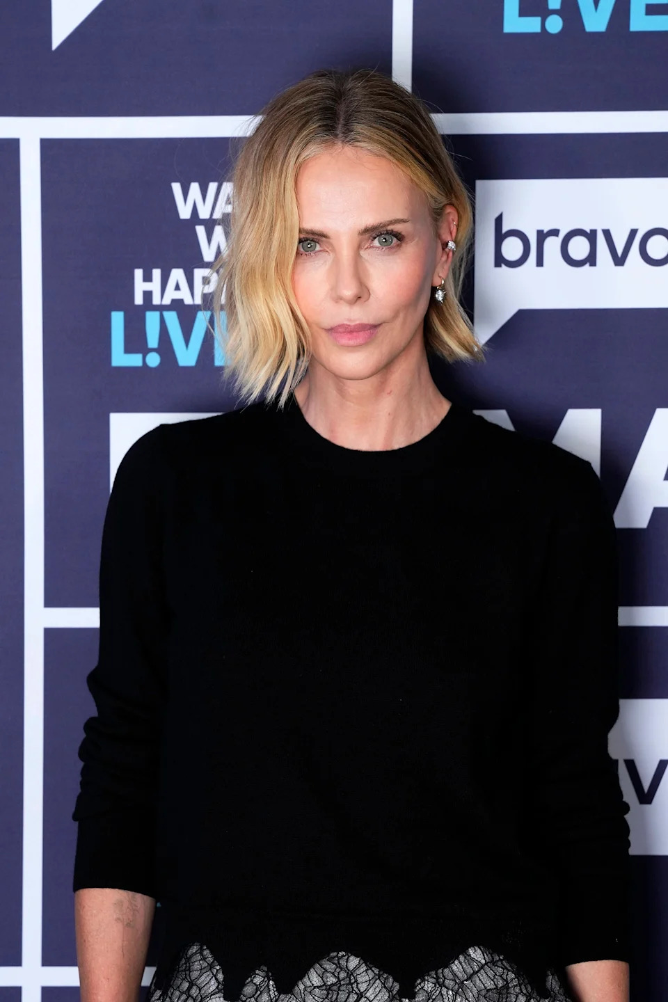Person with short blonde hair in a black top on a press event backdrop
