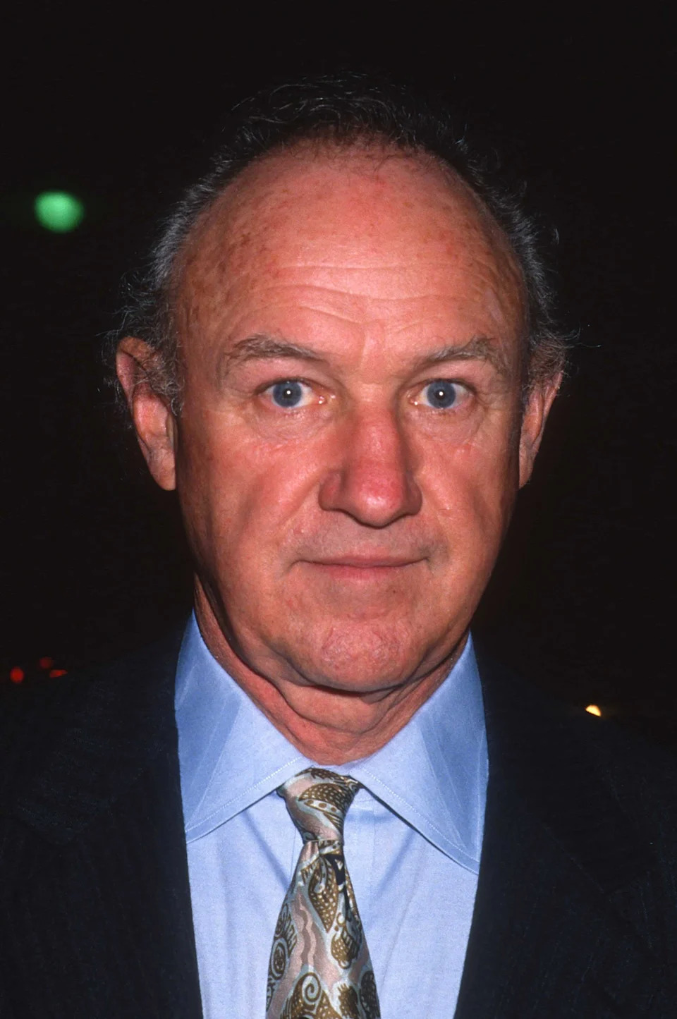 Gene Hackman wearing a suit with a patterned tie is looking at the camera