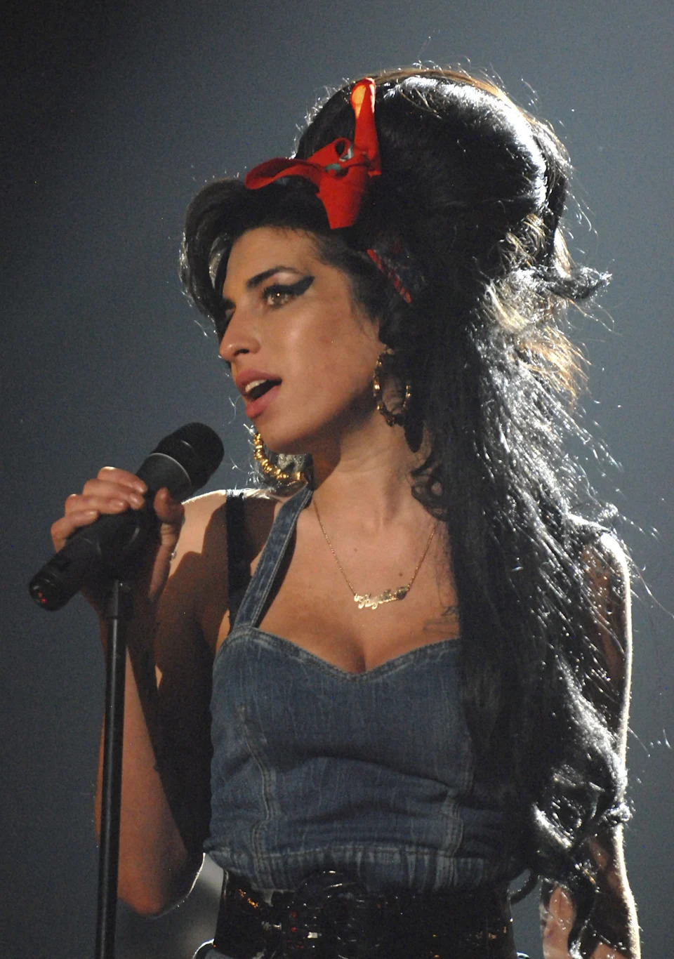 Singer performs passionately with a beehive hairstyle and denim outfit on stage, holding a microphone