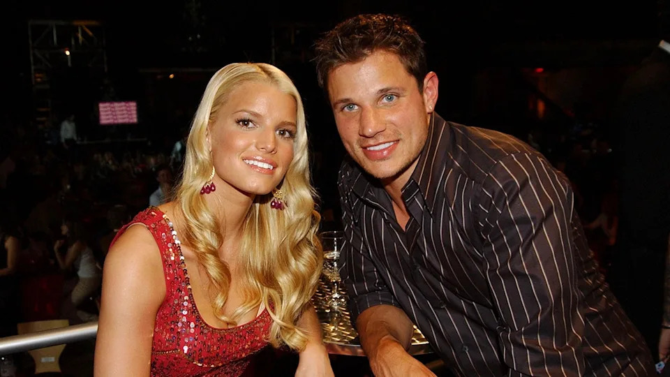 Jessica Simpson smiling in a sparkly red dress next to Nick Lachey in a black striped shirt at Hollywood Palladium