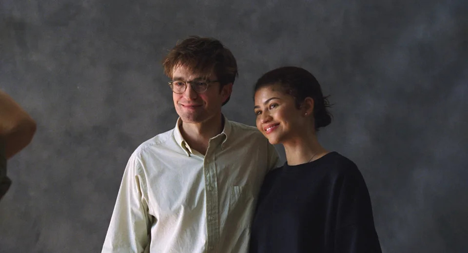 Two people pose together, smiling. One wears glasses and a light shirt, the other has a dark top