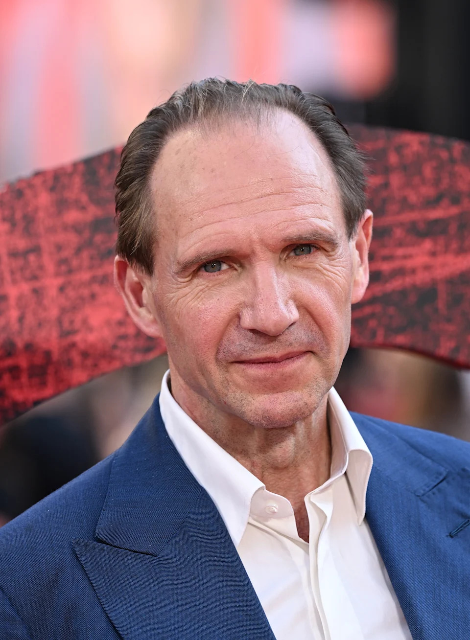 Actor in a tailored suit on the red carpet at a celebrity event, looking directly at the camera with a slight smile