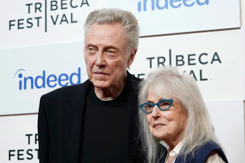 Two people pose at the Tribeca Festival. The person on the left wears a dark outfit, and the person on the right has long white hair and glasses