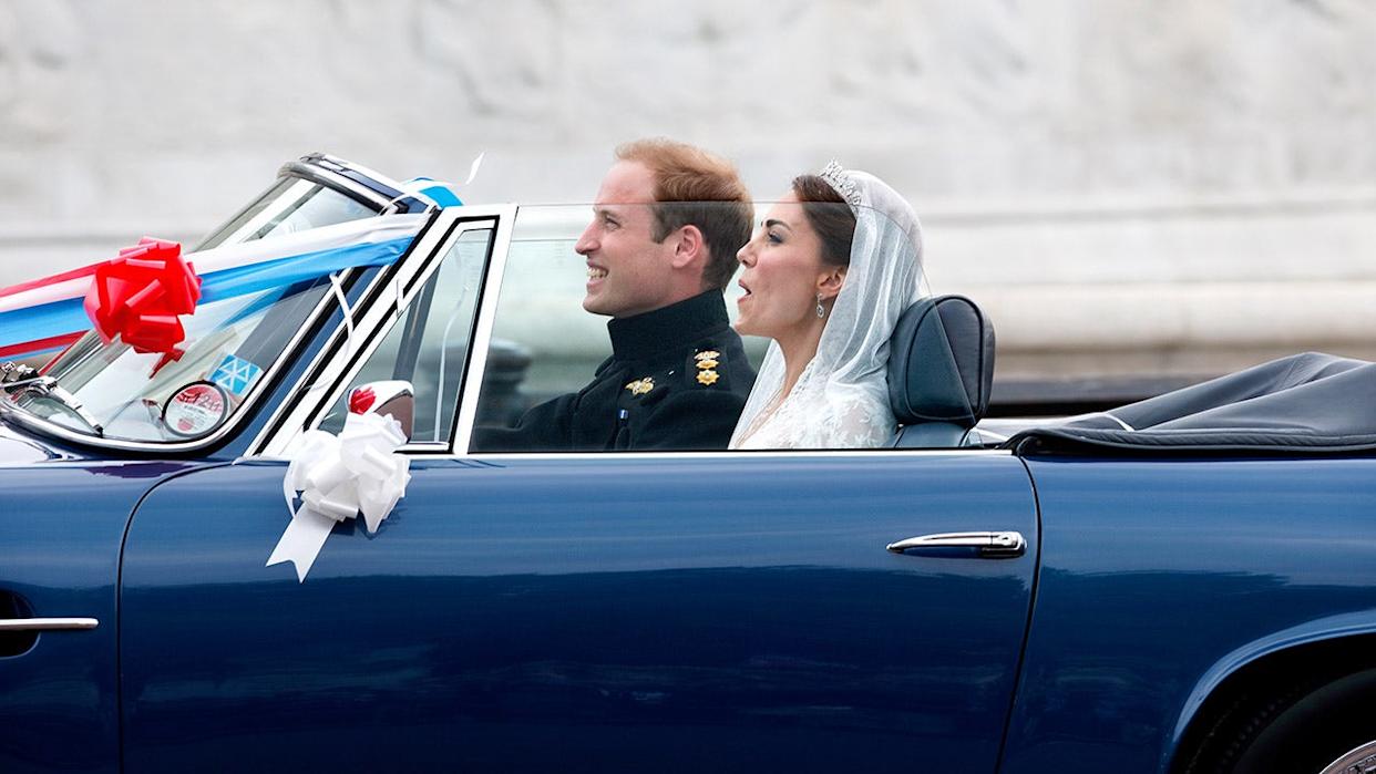 Prince William and Kate Middleton driving a blue Aston Martin convertible decorated with ribbons and balloons.