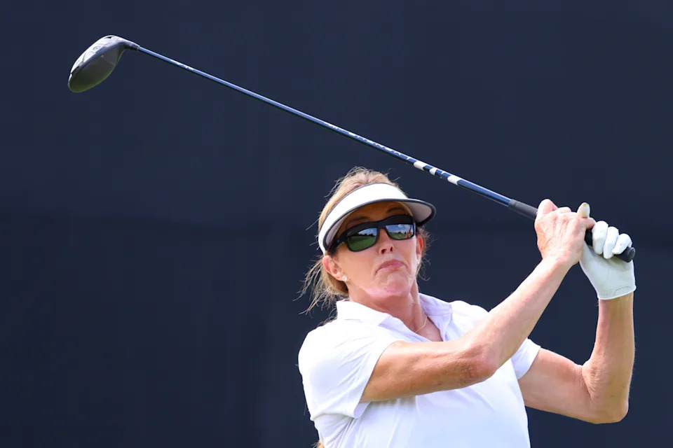 Caitlyn Jenner playing golf, wearing a visor and sunglasses, holding a golf club mid-swing on a sunny day