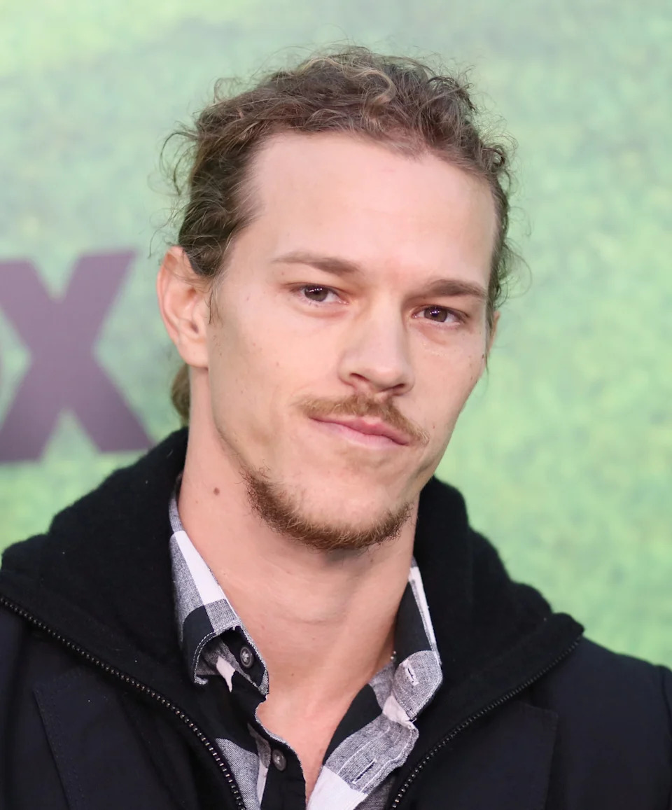 Ryan Dorsey with long hair pulled back, wearing a plaid shirt and a jacket, attending an event