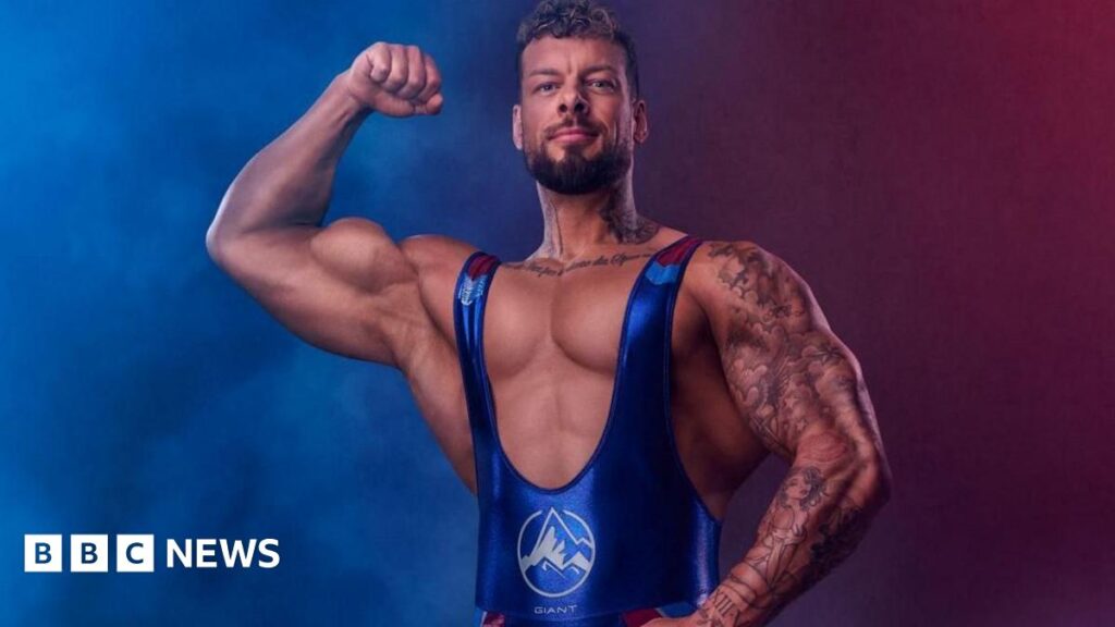 Giant in his Gladiators outfit. He is flexing his large biceps for the camera.