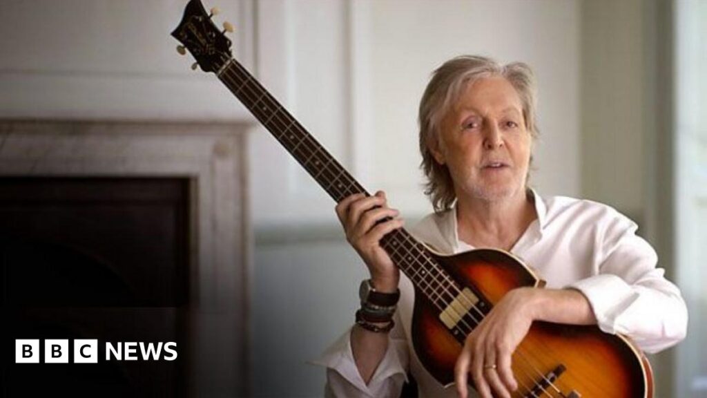 An image of Ian Horne, aged 79, sat at home on the sofa, looking into camera and wearing a white shirt and grey waistcoat.