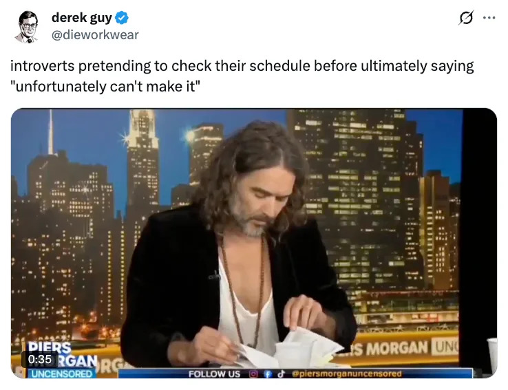 Man with long hair and casual open shirt reading papers on TV set with city skyline backdrop; tweet caption jokes about introverts making excuses