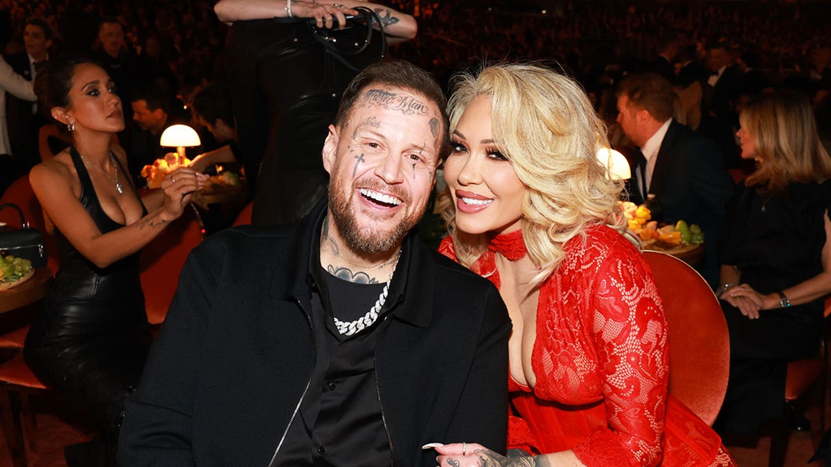Jelly Roll and Bunnie sitting together at a table smiling during the Grammy Awards.