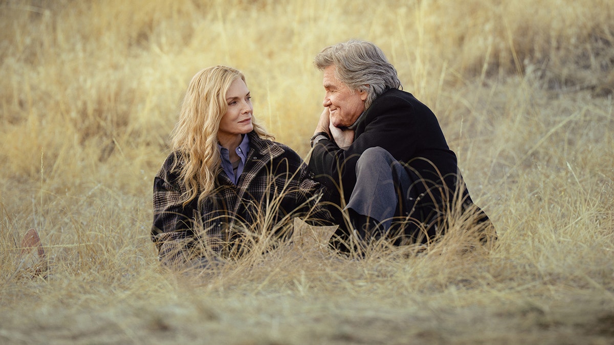 Michelle Pfeiffer and Kurt Russell sitting facing each other in tall dry grass