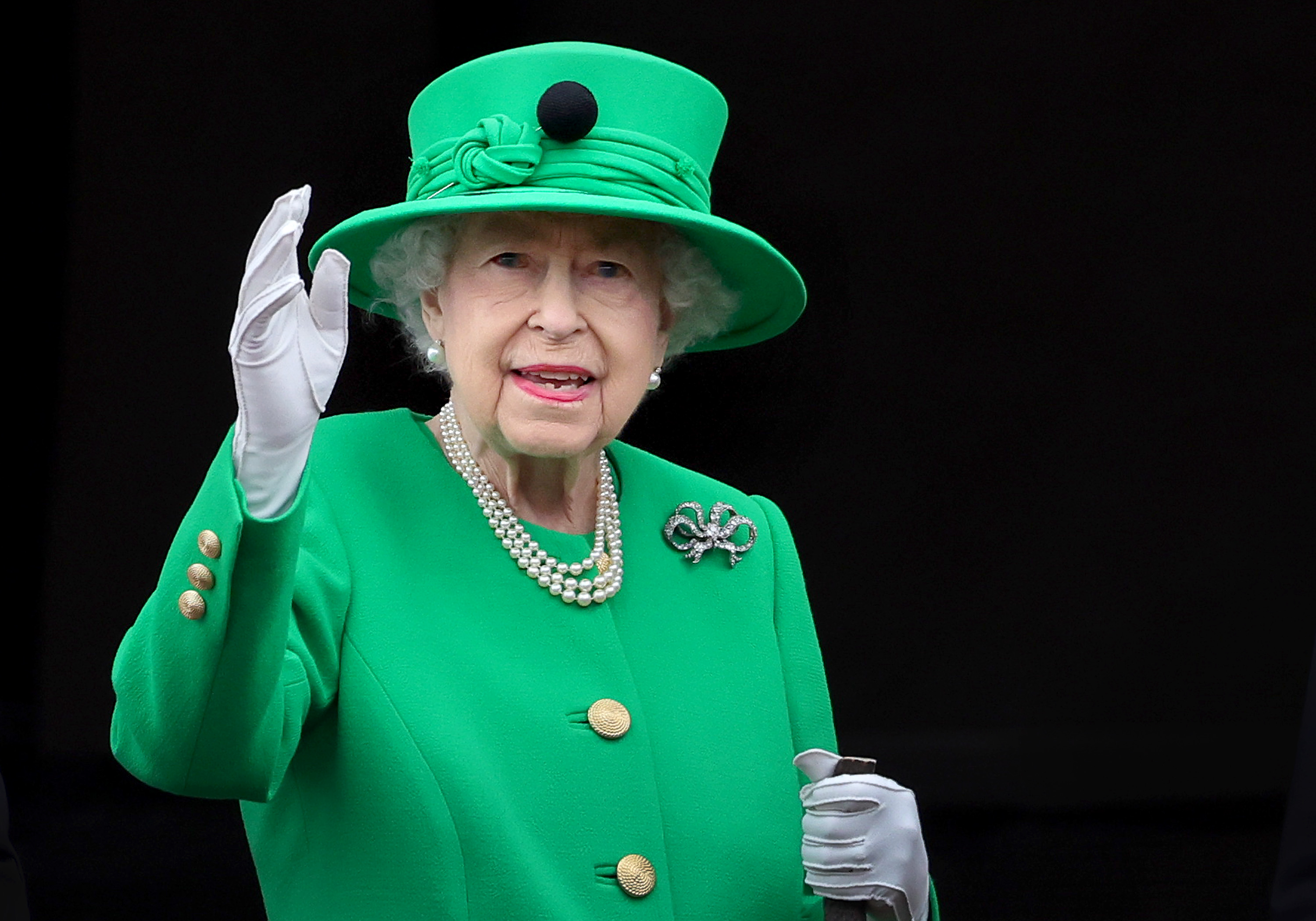 Queen Elizabeth wearing a green dress and hat waving