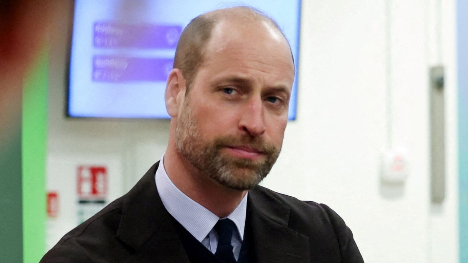 Prince William looks serious while wearing a shirt and tie, he has a beard and a balding hairline