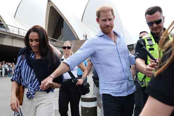 The Duke of Sussex puts out an arm as he and Meghan Markle stroll past Sydney Opera House