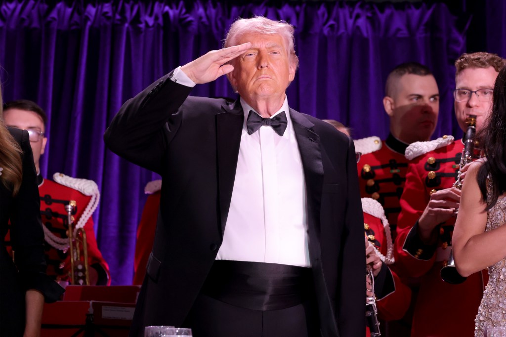 Donald Trump saluting while wearing a tuxedo, with musicians in red uniforms in the background.